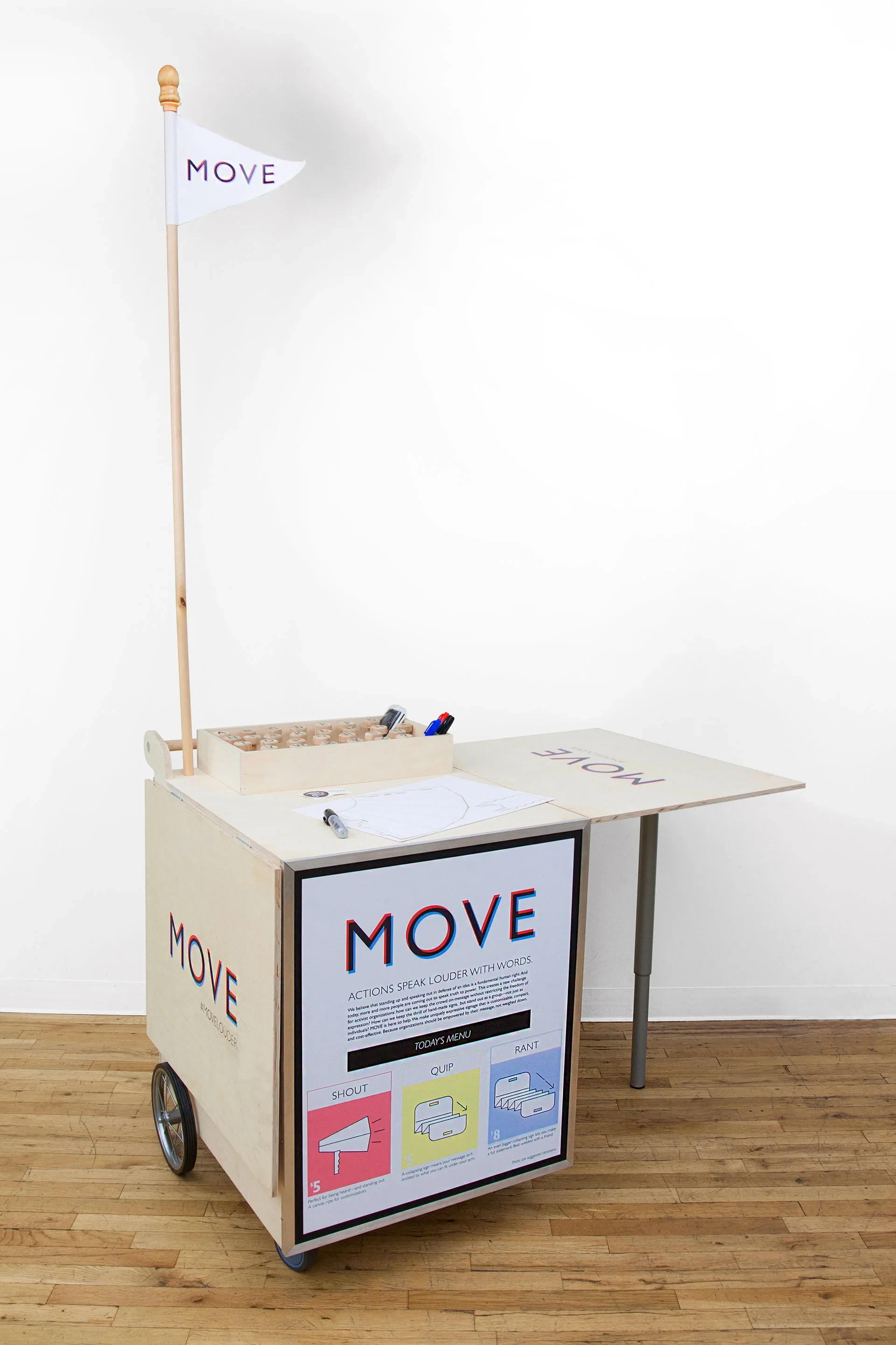 MOVE's mobile customization cart, unfolded with a pennant flag, stamps, pens, and a fold-out worktable