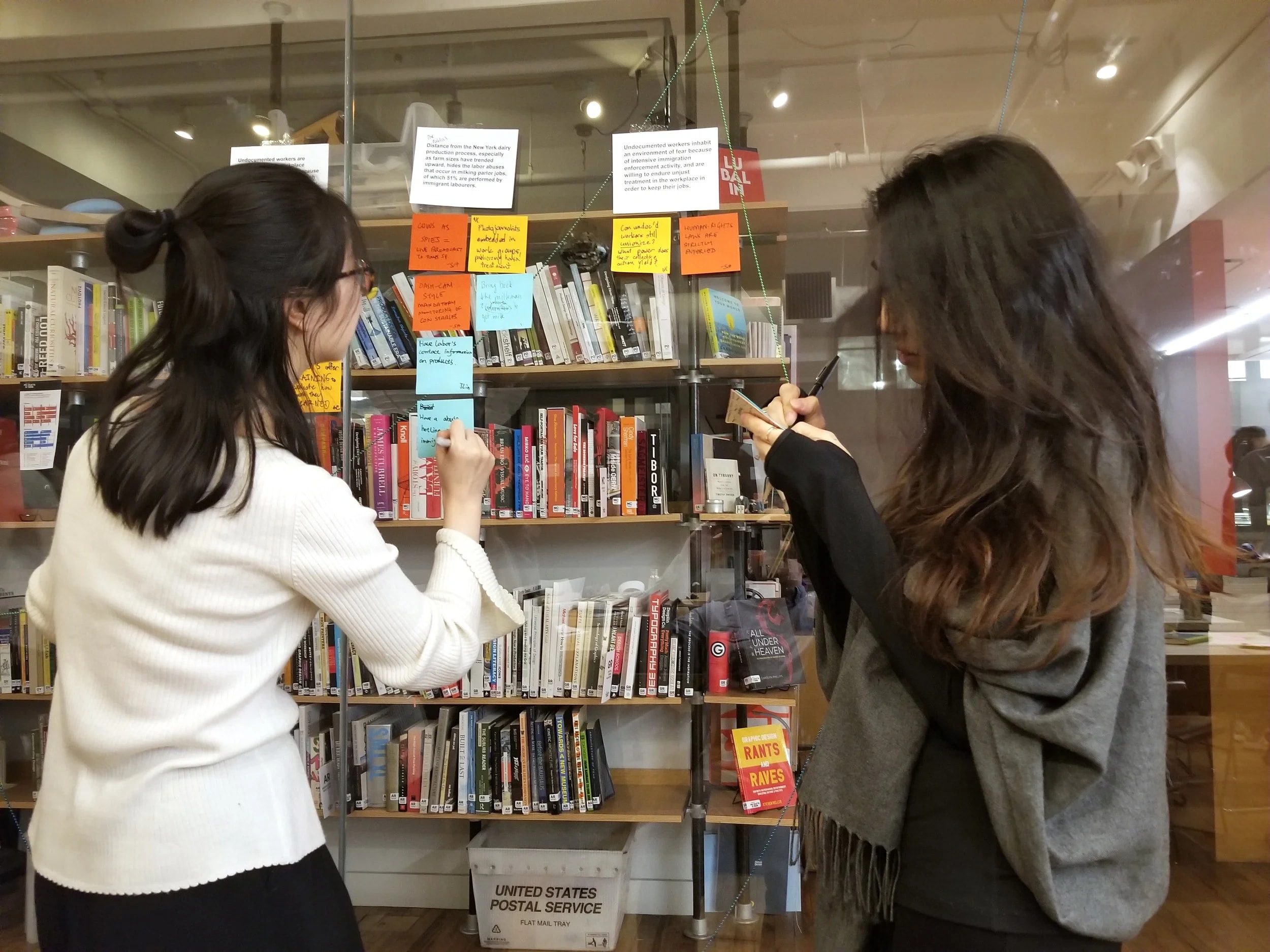 Classmates sorting brainstormed post-it notes into related directions on a library bookshelf